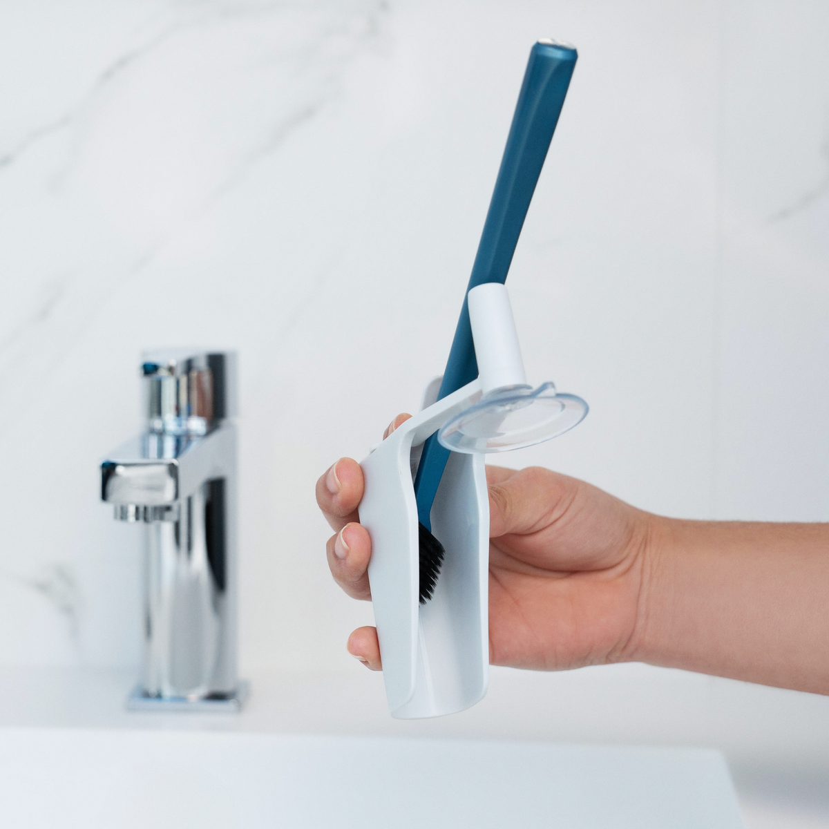 Hand holding a NOOK Toothbrush Holder with a manual toothbrush inside, next to a bathroom sink