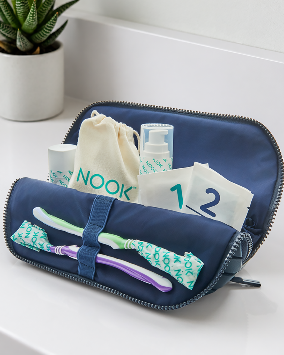 NOOK travel toiletry case open showing individually wrapped toothbrushes and travel bottles, vertical crop