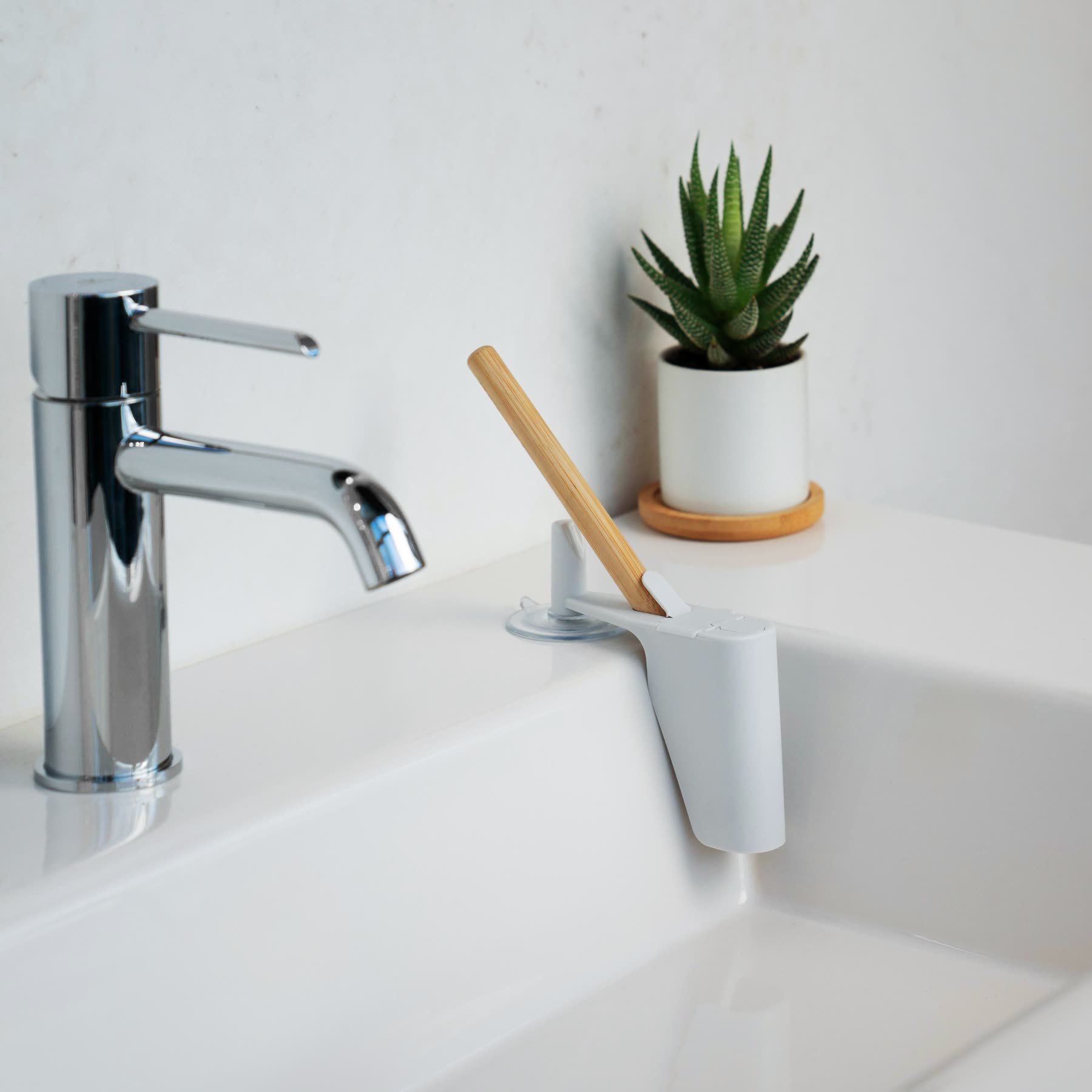 NOOK Electric Toothbrush Cover suction-mounted to a bathroom sink next to a small succulent