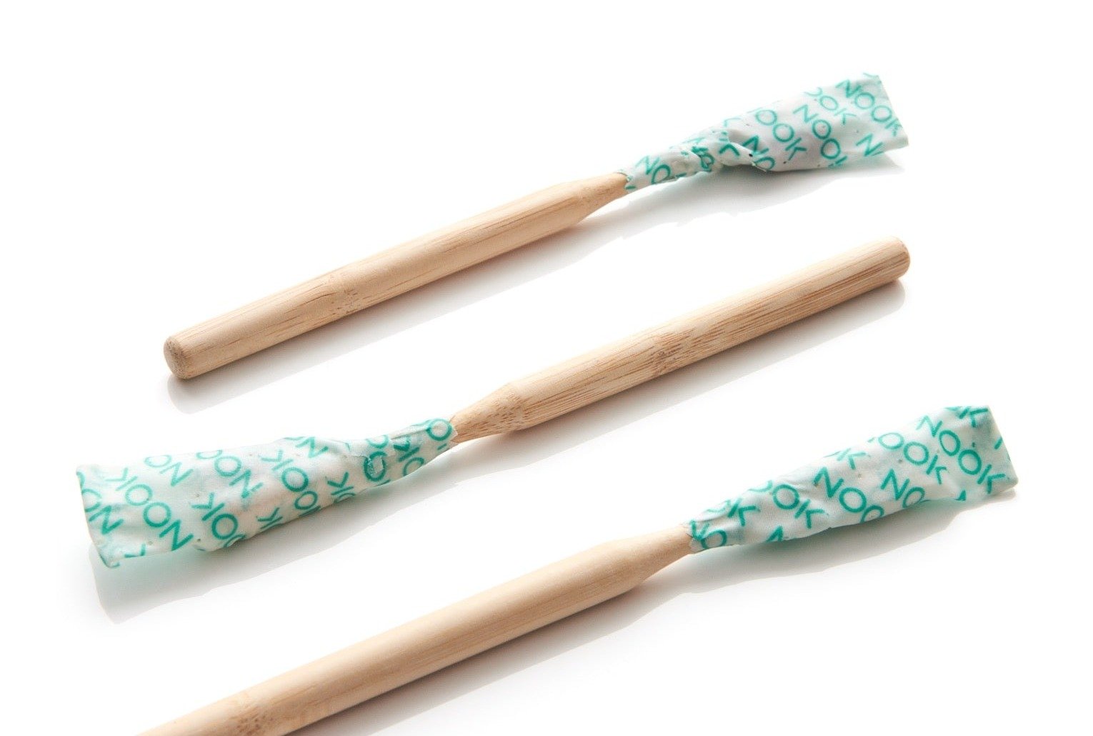 Three NOOK toothbrushes wrapped in NOOK-branded wipe-and-wrap fabric, arranged diagonally on a white background
